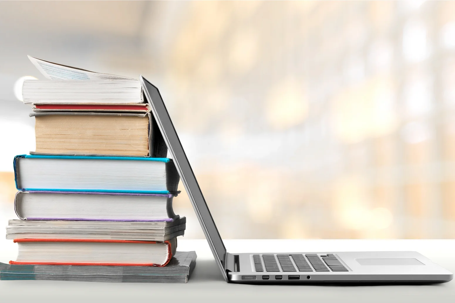 ein Laptop steht aufgeklappt vor einem Stapel von Büchern