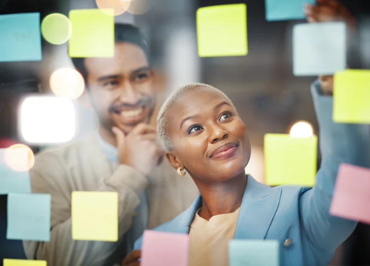 Frau steht an durchsichtiger Notizwand und bringt Post-Its an