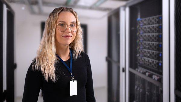Systemadministratorin steht in einem Serverraum neben mehreren Server-Racks.